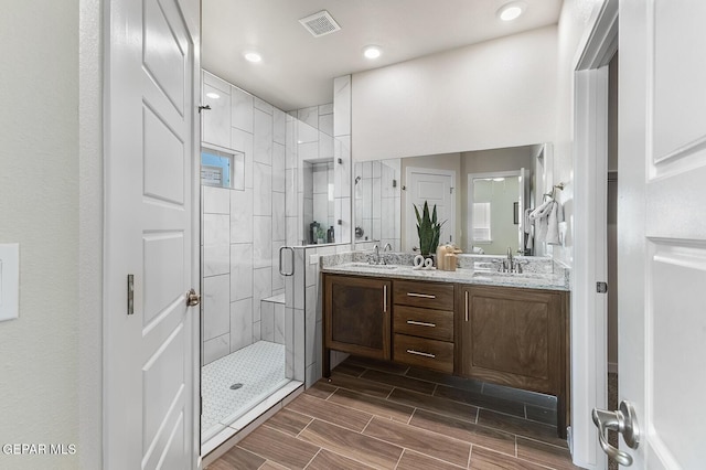 full bathroom with a shower stall, double vanity, a sink, and visible vents