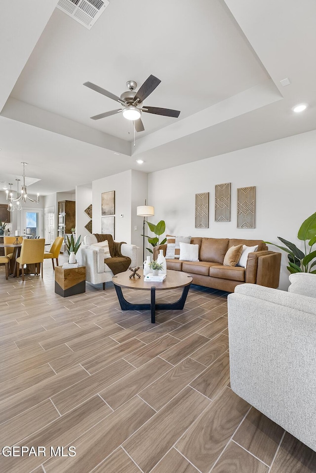 living room with a raised ceiling, ceiling fan with notable chandelier, visible vents, and recessed lighting