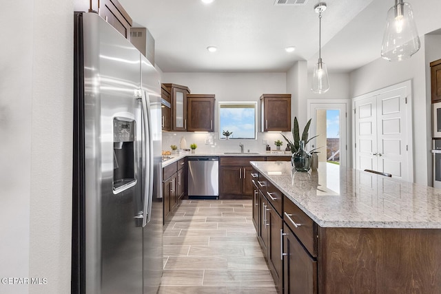 kitchen featuring light stone counters, a center island, decorative light fixtures, decorative backsplash, and appliances with stainless steel finishes