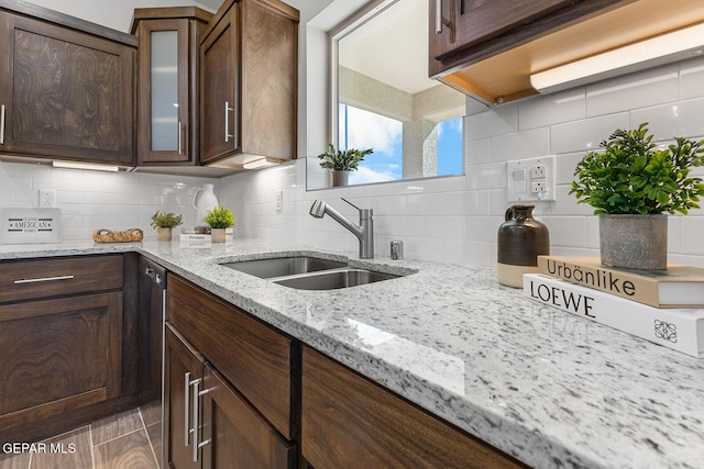 kitchen featuring glass insert cabinets, dark brown cabinetry, light stone counters, a sink, and decorative backsplash