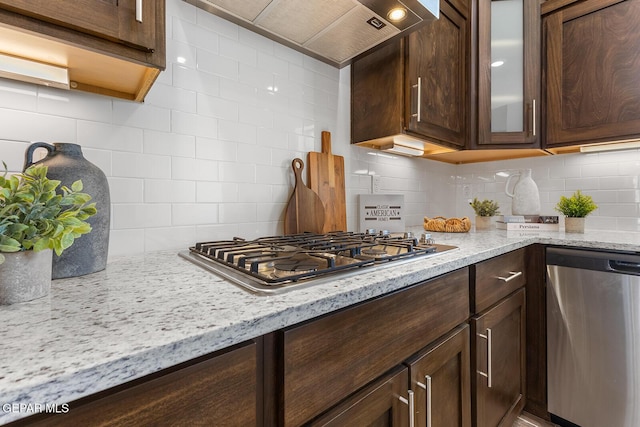 kitchen with glass insert cabinets, dark brown cabinetry, custom range hood, stainless steel appliances, and decorative backsplash