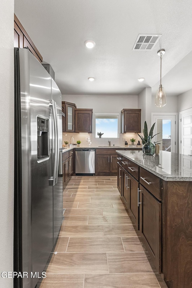 kitchen featuring light stone counters, a center island, dark brown cabinets, visible vents, and appliances with stainless steel finishes