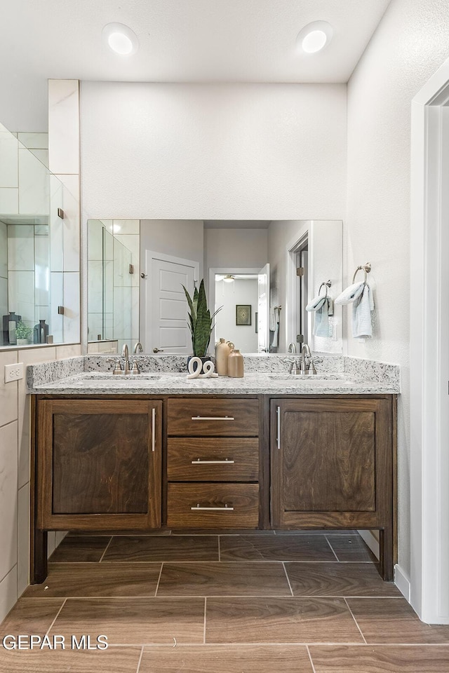 bathroom featuring double vanity, a sink, a stall shower, and wood tiled floor