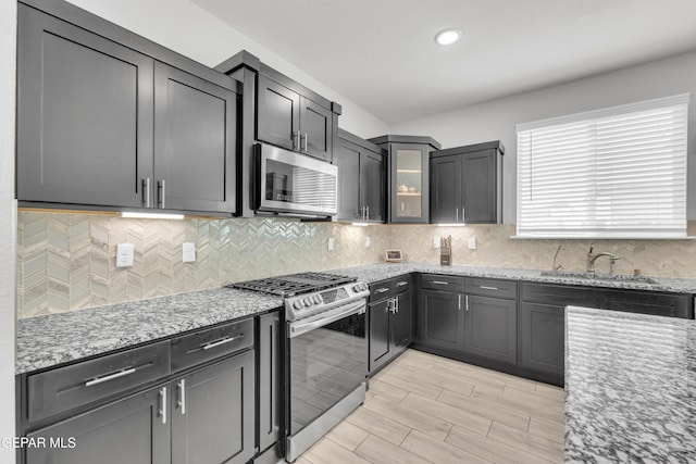 kitchen with a sink, decorative backsplash, light stone countertops, and stainless steel appliances