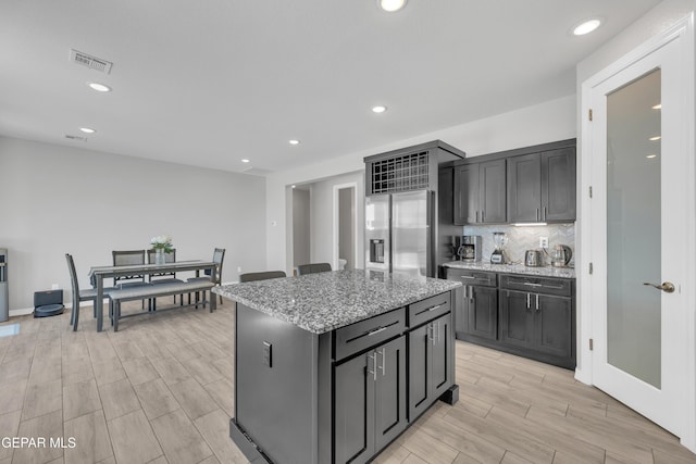 kitchen featuring recessed lighting, light wood-style flooring, a kitchen island, stainless steel refrigerator with ice dispenser, and decorative backsplash