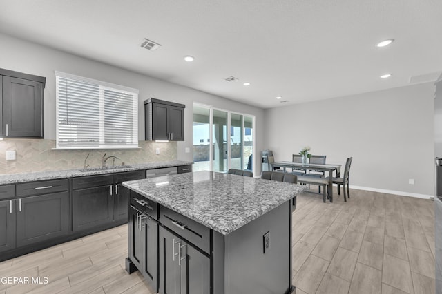 kitchen with tasteful backsplash, visible vents, a center island, a sink, and light wood-style flooring