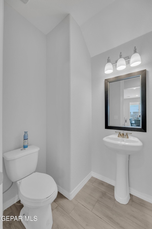 half bathroom with a sink, toilet, wood finish floors, and baseboards