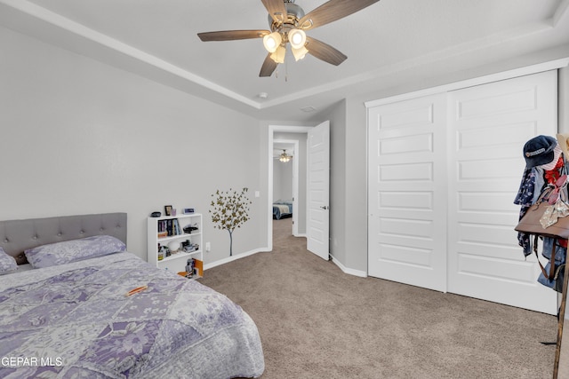 bedroom featuring ceiling fan, carpet, a closet, a raised ceiling, and baseboards