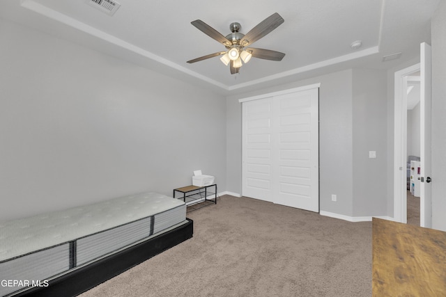 unfurnished bedroom featuring a closet, visible vents, carpet floors, a raised ceiling, and baseboards
