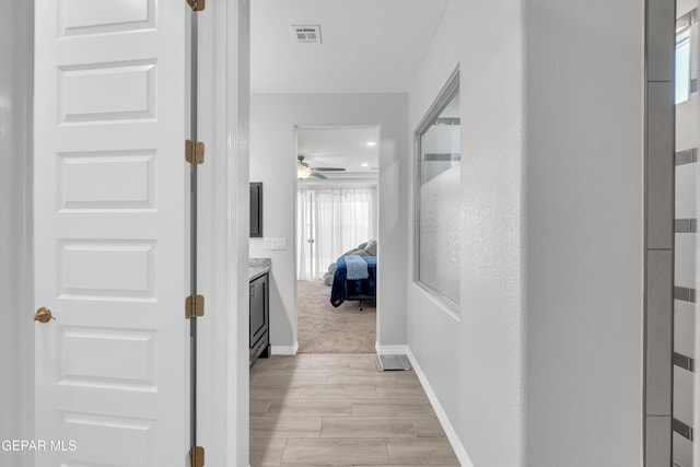 hall featuring light wood-type flooring, baseboards, and visible vents