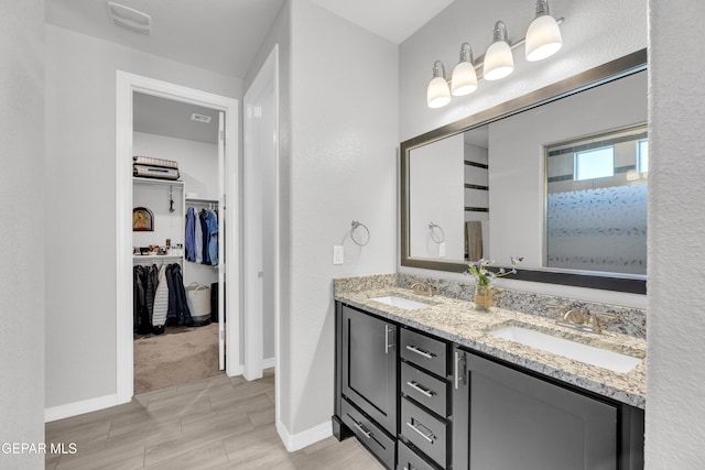 full bathroom featuring baseboards, double vanity, a sink, and a walk in closet