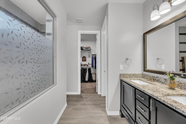 full bath with double vanity, a sink, a spacious closet, and baseboards
