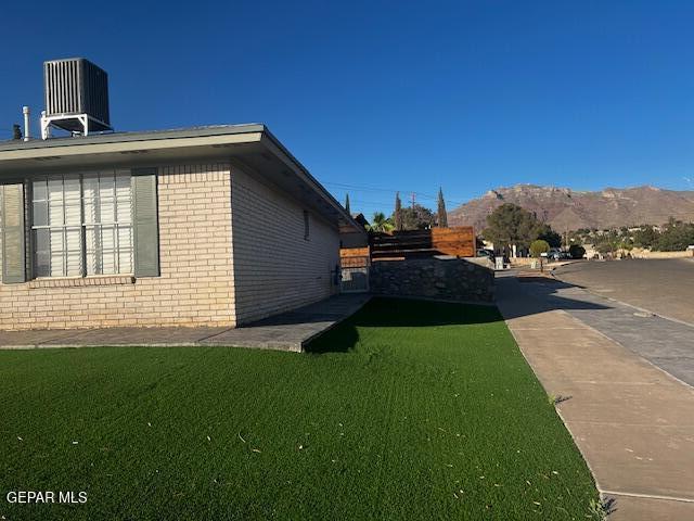 view of side of property featuring brick siding, a lawn, central AC unit, and a mountain view