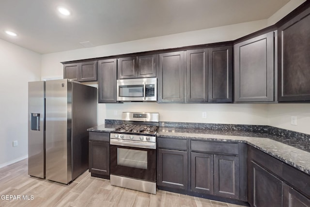 kitchen with dark brown cabinets, light wood-style flooring, dark stone counters, and stainless steel appliances