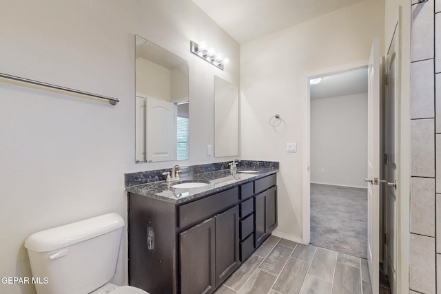 bathroom with toilet, double vanity, a sink, and baseboards