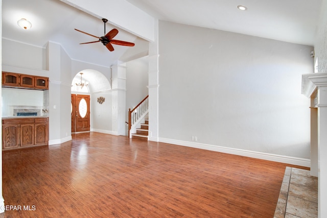 unfurnished living room with ceiling fan with notable chandelier, high vaulted ceiling, beamed ceiling, arched walkways, and baseboards