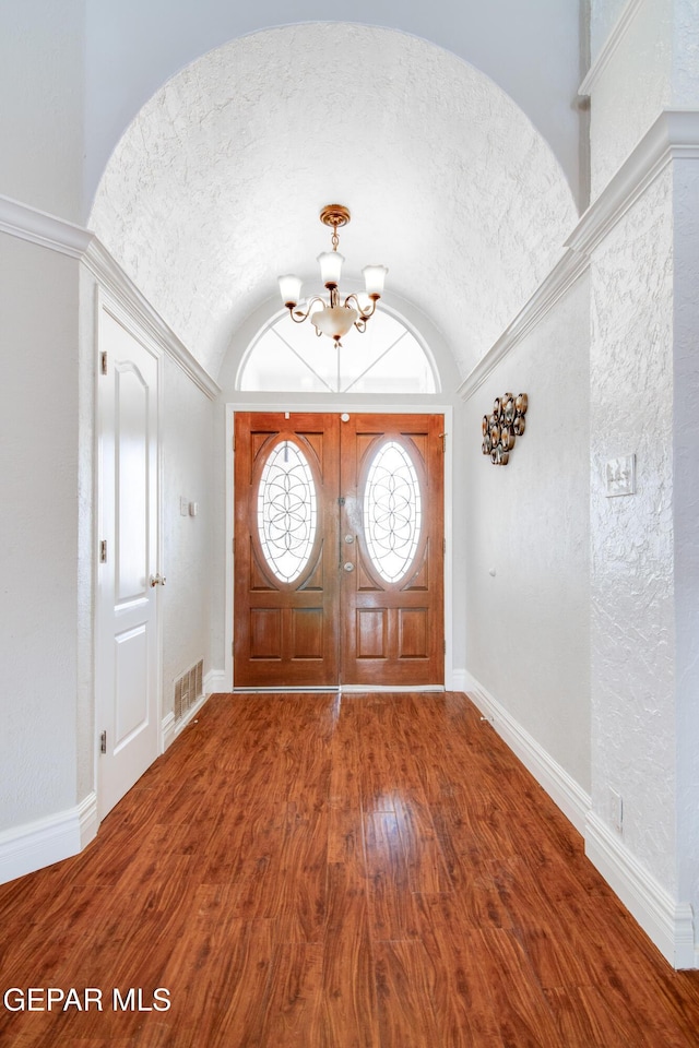 foyer entrance featuring baseboards, wood finished floors, a chandelier, and vaulted ceiling