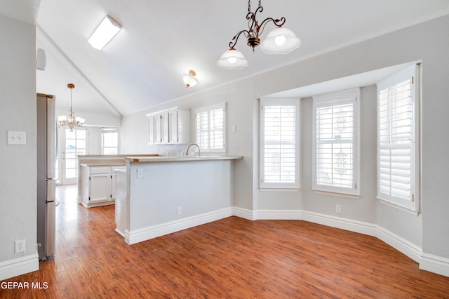 kitchen with a chandelier, a peninsula, freestanding refrigerator, white cabinets, and wood finished floors