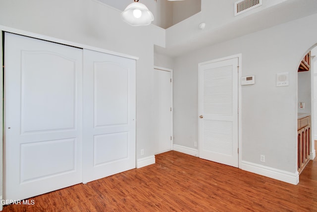 unfurnished bedroom with arched walkways, visible vents, baseboards, and wood finished floors