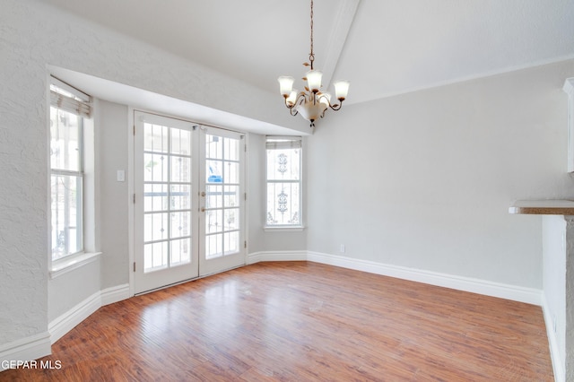 unfurnished dining area featuring french doors, an inviting chandelier, wood finished floors, and a wealth of natural light