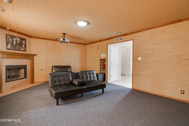 living area with visible vents, ornamental molding, a textured ceiling, carpet floors, and a tile fireplace