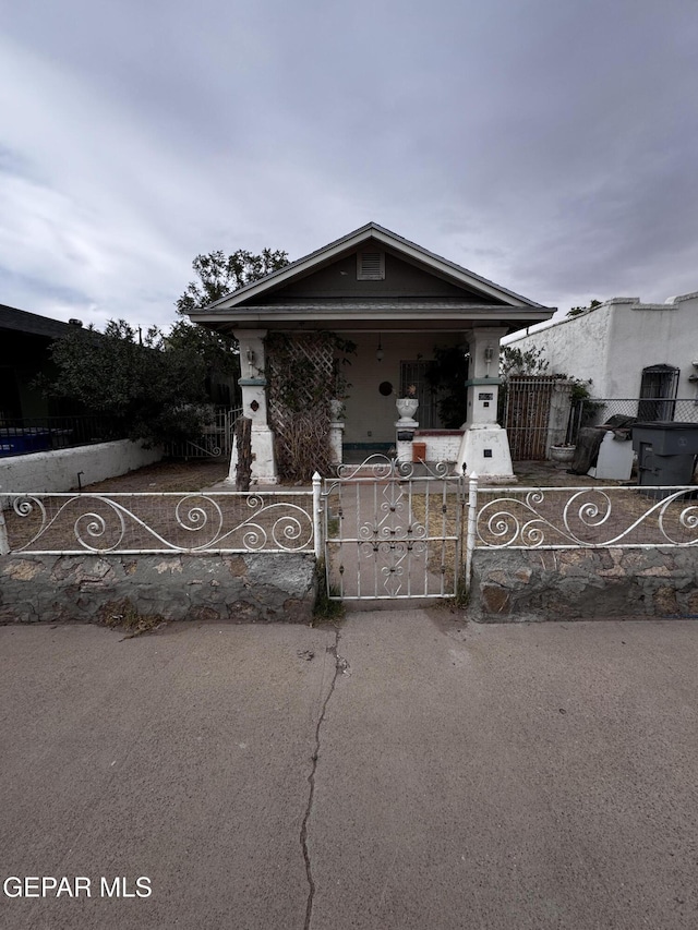 shotgun-style home featuring a porch, a gate, and a fenced front yard