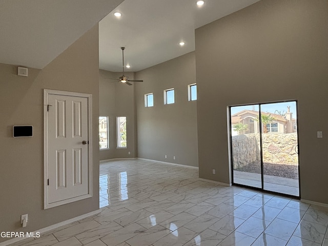 empty room with baseboards, marble finish floor, a towering ceiling, and a wealth of natural light