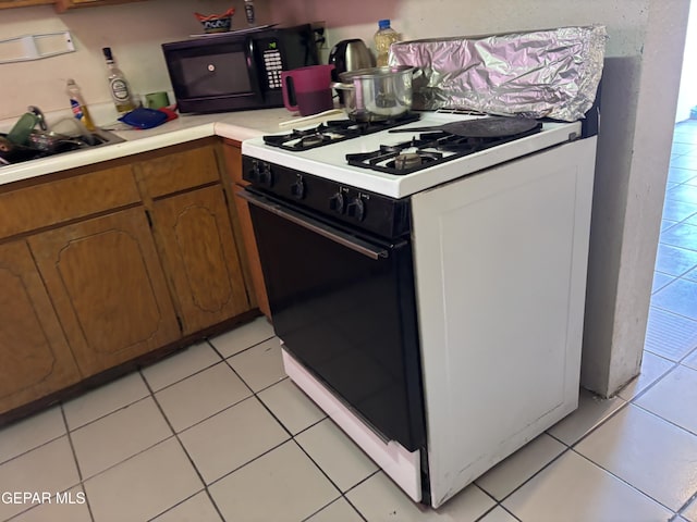 8154 Holloway Pl, El Paso, TX 79907 - kitchen featuring light countertops, black microwave, brown cabinetry, gas stove, and light tile patterned flooring