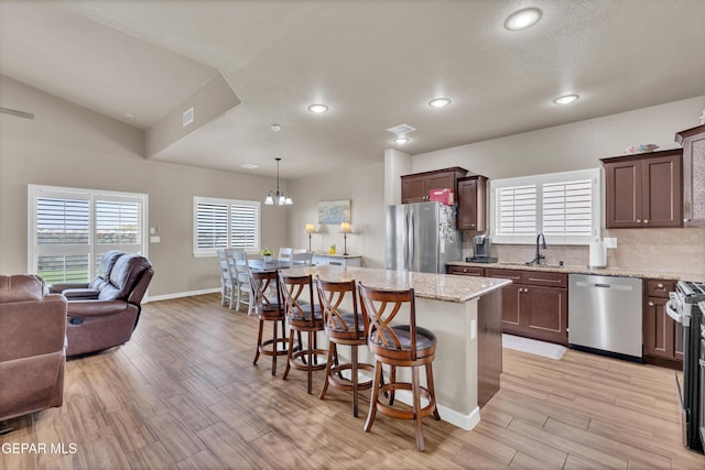 3841 Loma Adriana, El Paso, TX 79938 - kitchen with appliances with stainless steel finishes, open floor plan, a kitchen breakfast bar, light wood-style floors, and a kitchen island