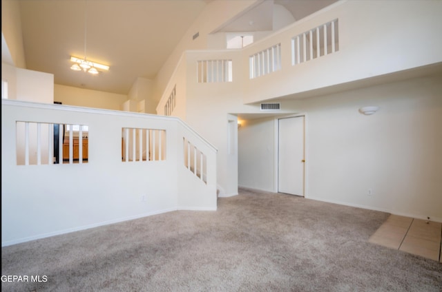 unfurnished living room featuring visible vents, baseboards, carpet floors, stairway, and a towering ceiling