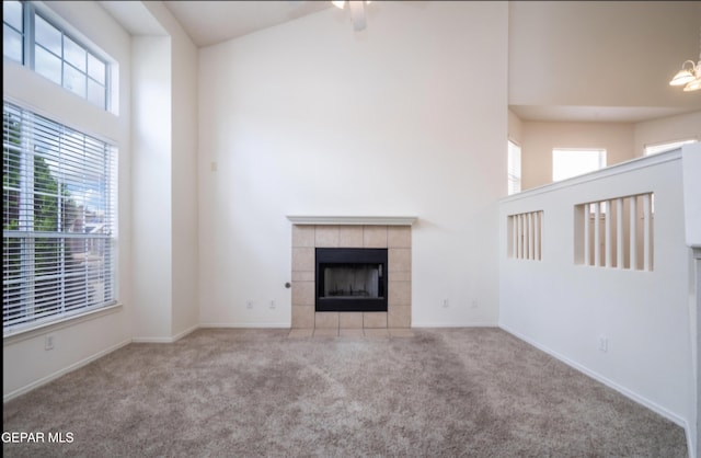 unfurnished living room with carpet flooring, a tile fireplace, a high ceiling, and baseboards