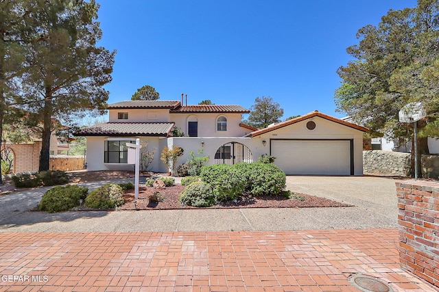 mediterranean / spanish-style home featuring a tile roof, decorative driveway, fence, a garage, and stucco siding
