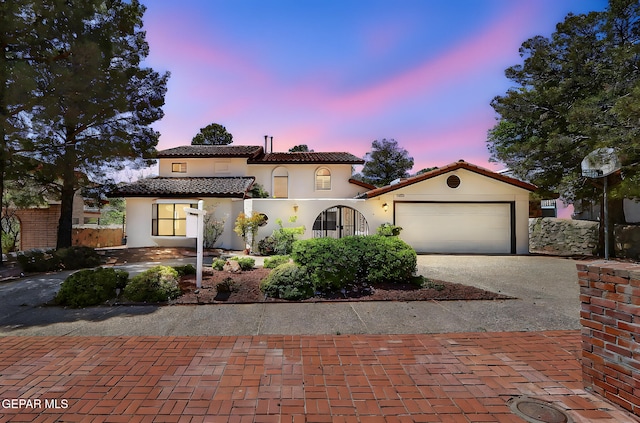 mediterranean / spanish home with stucco siding, a tiled roof, a garage, and decorative driveway