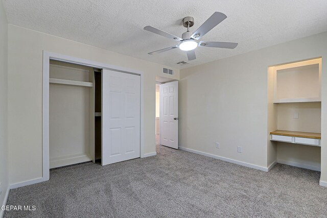 unfurnished bedroom featuring a textured ceiling, a closet, built in desk, carpet flooring, and visible vents