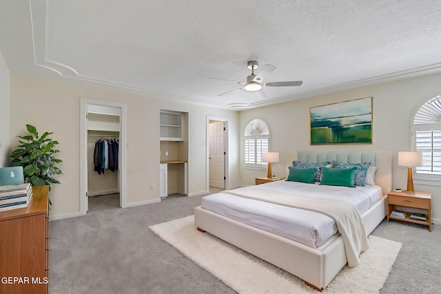 bedroom with light colored carpet, baseboards, a walk in closet, and a textured ceiling