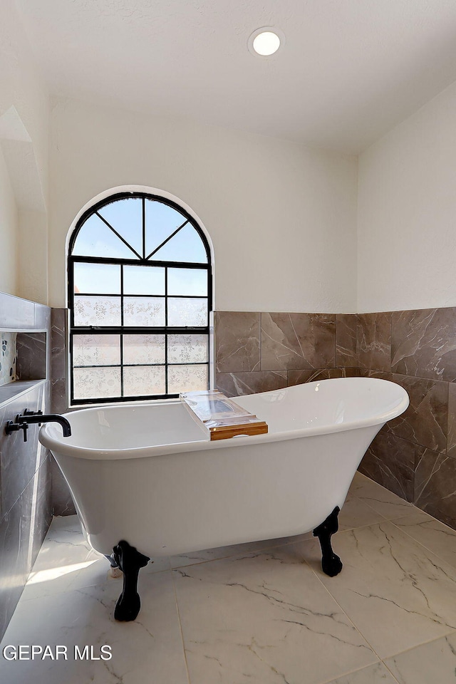 bathroom featuring tile walls, marble finish floor, a wainscoted wall, a soaking tub, and recessed lighting