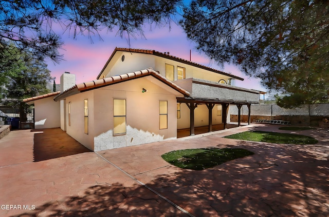 rear view of property featuring a chimney, a tiled roof, fence, a patio, and stucco siding