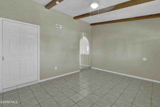 spare room with a ceiling fan, light tile patterned flooring, beamed ceiling, baseboards, and visible vents