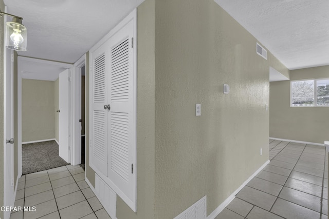 corridor with baseboards, a textured wall, visible vents, and light tile patterned floors