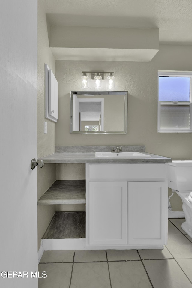 half bathroom featuring a textured wall, tile patterned flooring, vanity, and toilet