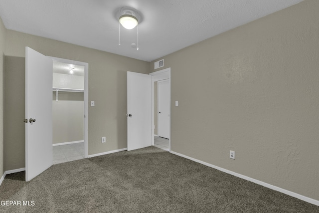 unfurnished bedroom featuring a closet, a spacious closet, carpet floors, baseboards, and visible vents