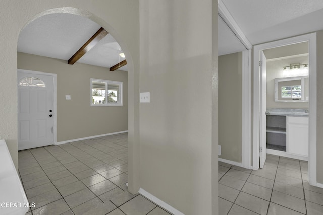 entryway with light tile patterned flooring, arched walkways, baseboards, and beamed ceiling