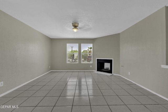 unfurnished living room with baseboards, a fireplace, ceiling fan, and light tile patterned flooring