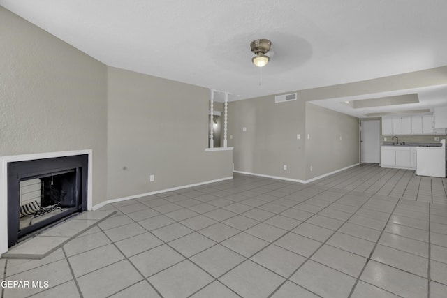 unfurnished living room featuring visible vents, a ceiling fan, light tile patterned floors, baseboards, and a fireplace