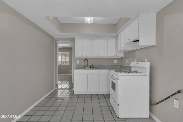 kitchen featuring white gas stove, a sink, light tile patterned floors, light countertops, and white cabinets