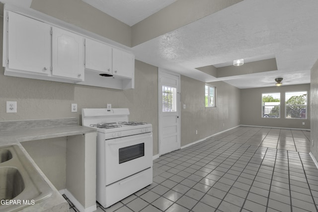 kitchen with white gas stove, a textured ceiling, open floor plan, light countertops, and white cabinets