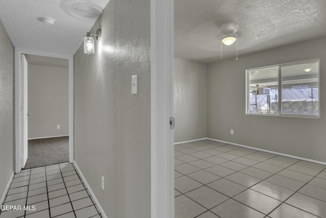hallway with baseboards, a textured wall, a textured ceiling, and light tile patterned floors