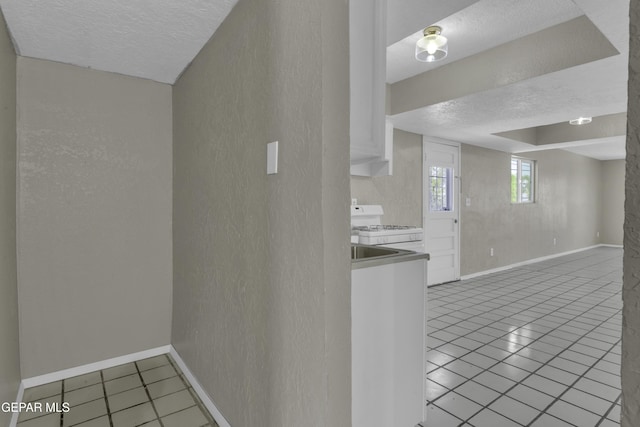 interior space featuring a textured wall, white range with gas stovetop, light tile patterned flooring, baseboards, and a textured ceiling