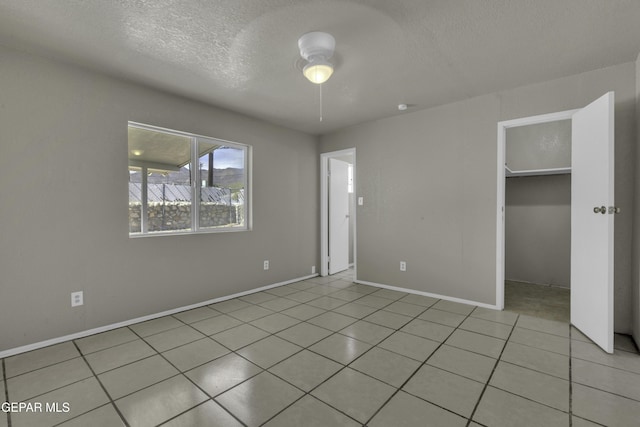 unfurnished bedroom with light tile patterned floors, baseboards, a textured ceiling, and a walk in closet