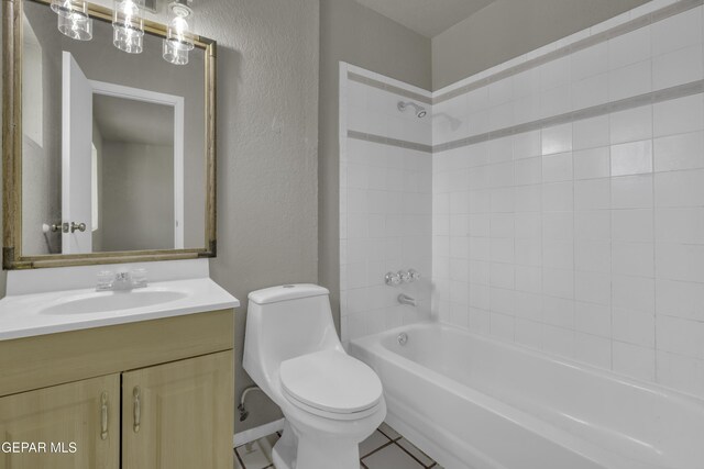 full bath with tile patterned floors, vanity, a textured wall, shower / bath combination, and toilet